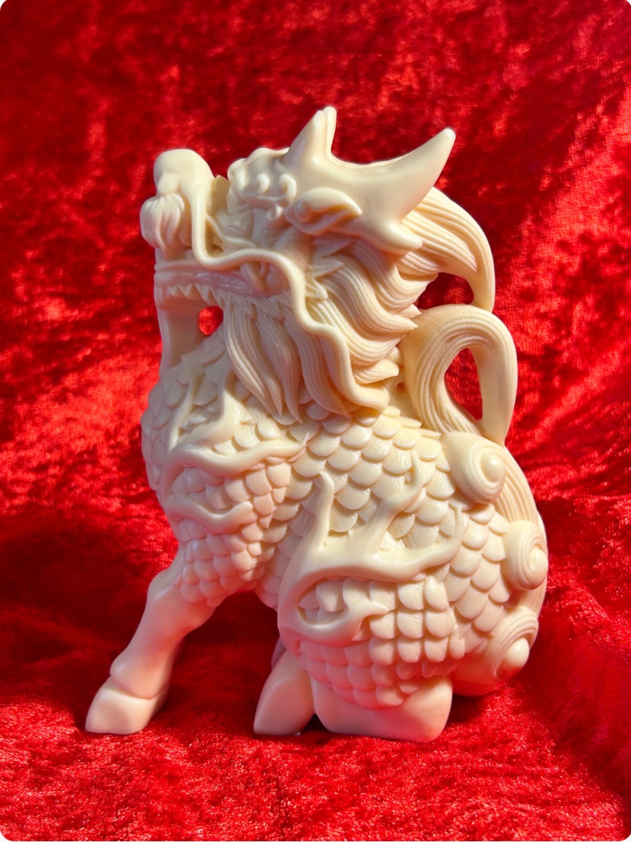 Rear three-quarter view of a 5-inch cream-coloured Chinese dragon figurine made f rom ivory nut composite, showing its curled tail, intricate scales, flowing mane and horns against red velvet.
