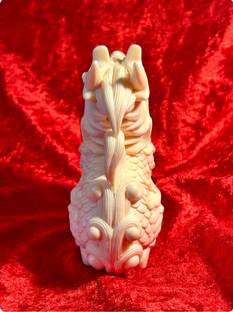Rear view of a 5-inch cream-coloured Chinese dragon figurine made from ivory nut composite, showing detailed horns, flowing man, textured scales and decorative tail against red velvet.