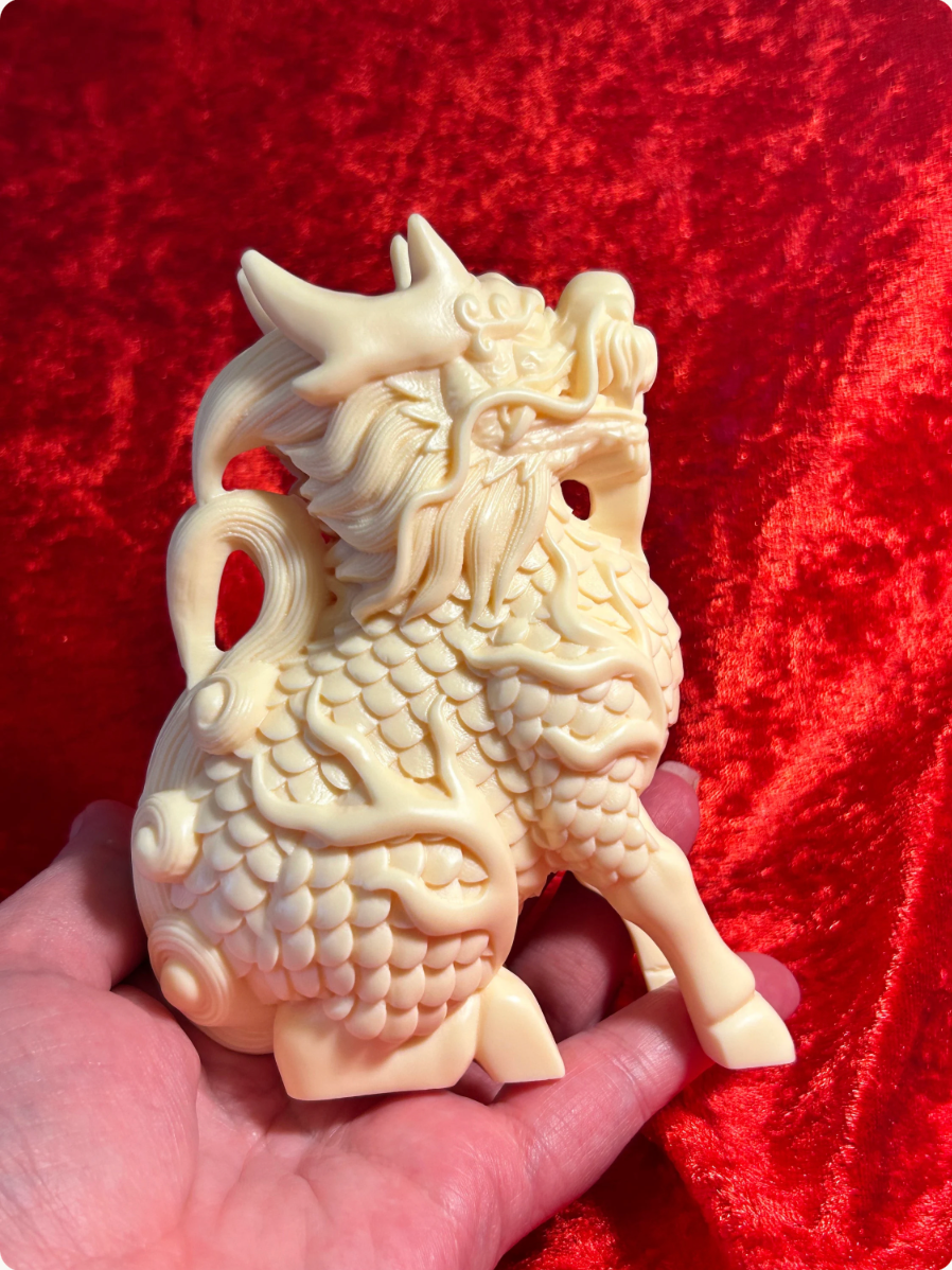 A hand holds a detailed, cream-colored Chinese Shishi guardian statue against a textured red velvet background.