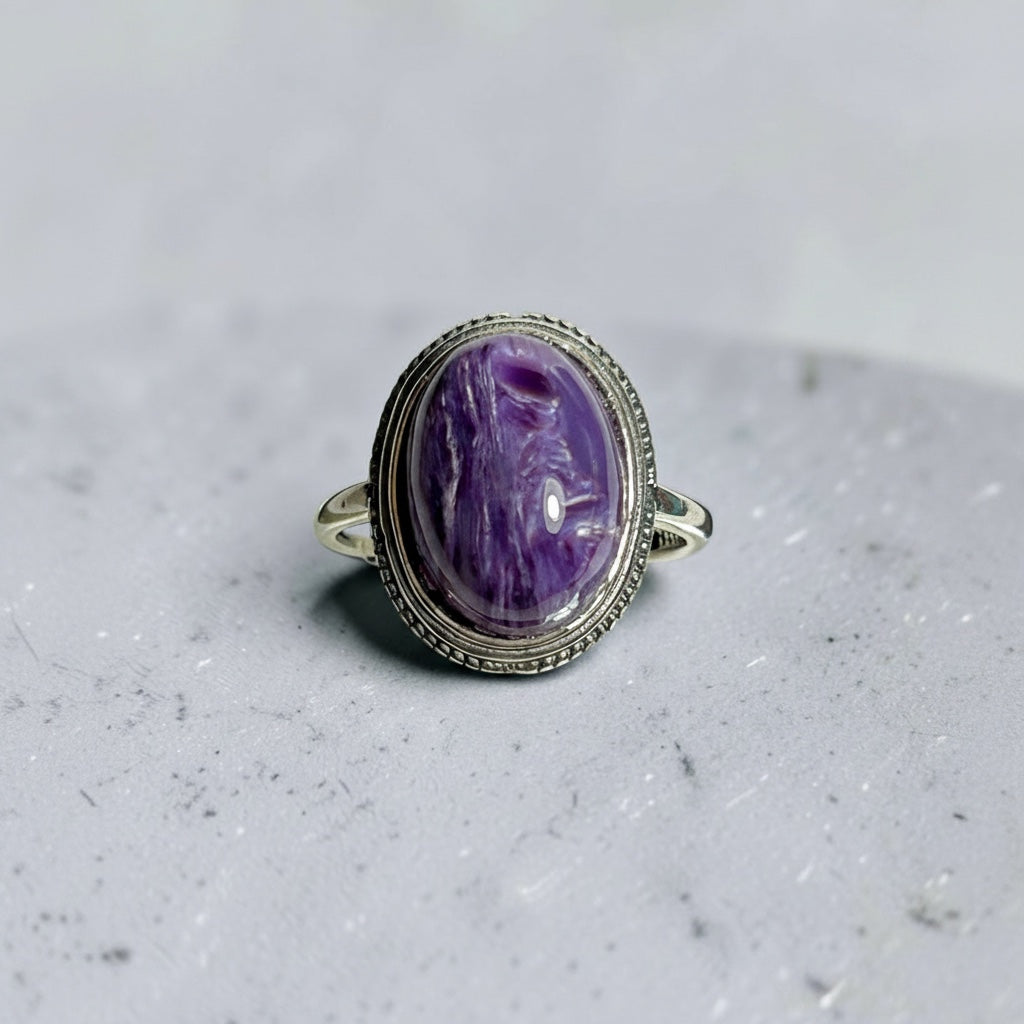 Celtic Dragon Jewellery adjustable sterling silver ring featuring an oval, bezel-set charoite cabochon with swirling purple patterns.